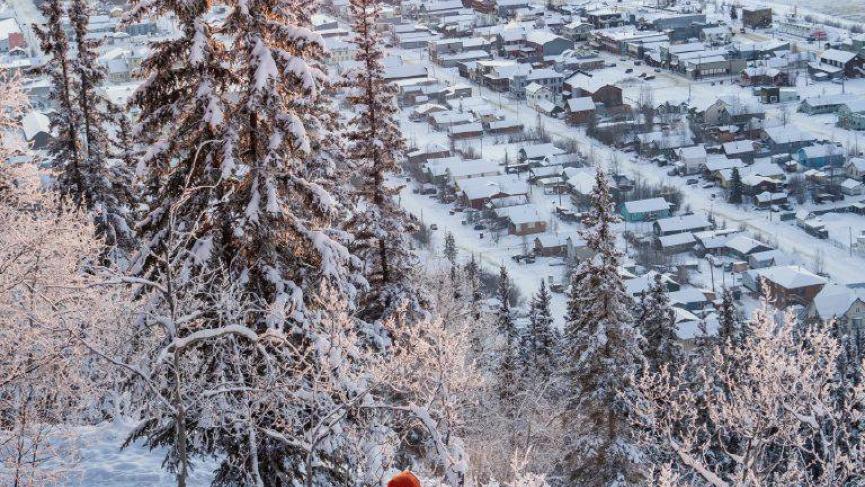 A hiker in a red jacket makes their way down a snowy mountain toward Dawson City
