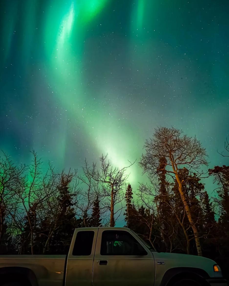 Northern lights dance above a parked vehicle