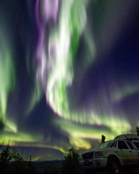 Purple, green and white northern lights swirl above a truck